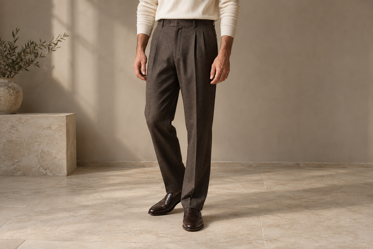 Detail of brown pleated work trousers with a flat waistband and tidy hems above dark loafers.