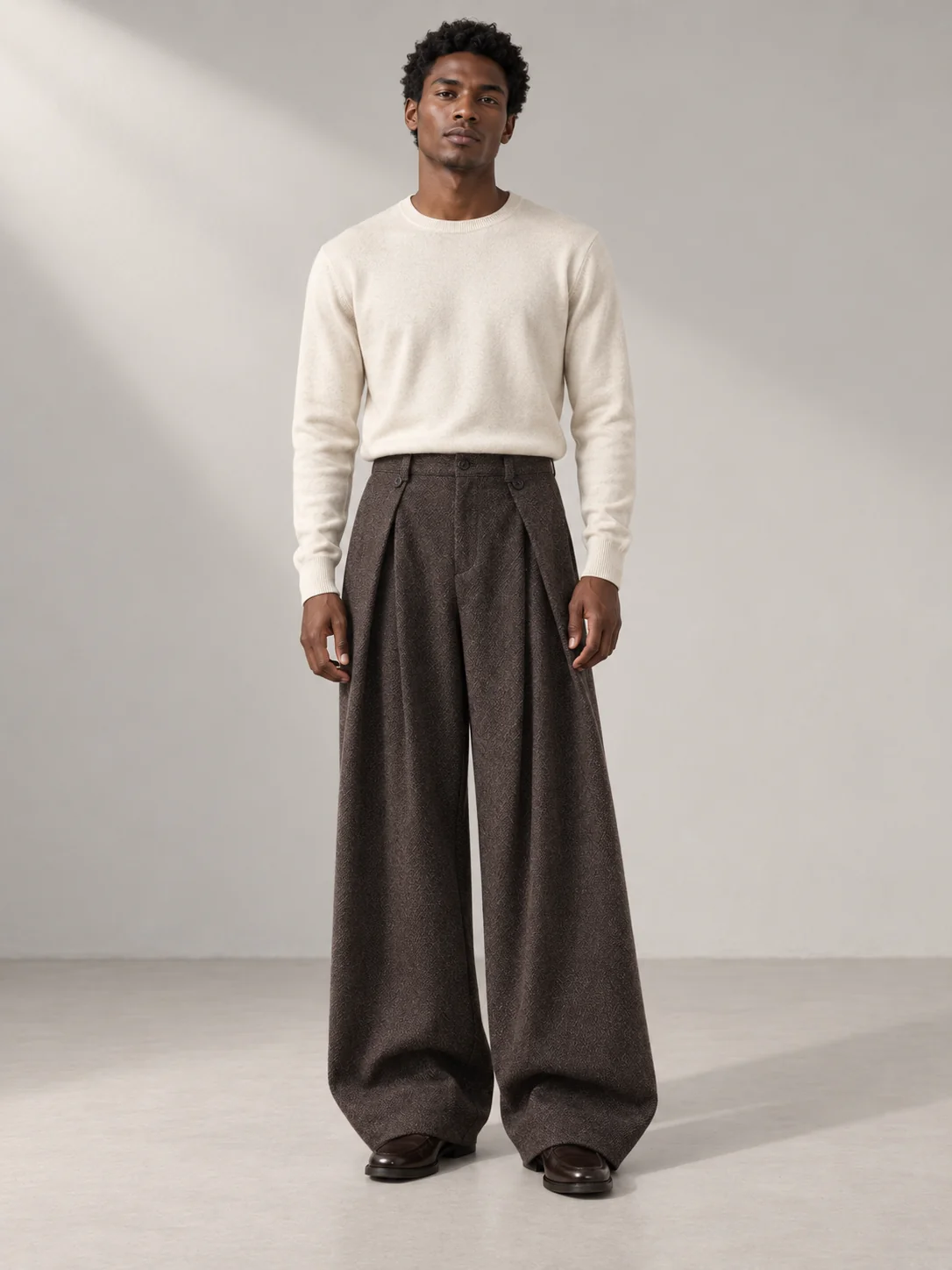 Model wearing an ivory knit sweater and brown wide-leg pleated trousers in a neutral studio.